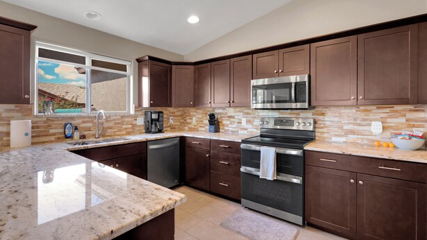 A modern kitchen with dark brown cabinets, stainless steel appliances, a large island, and a window providing natural light. - Beautiful 4-bedroom house with Pool in Tucson (Tucson)