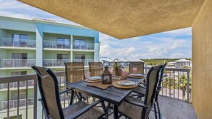 A balcony with a table set for four, surrounded by chairs, overlooking a building with multiple balconies. - Hot Tub•Oceanfront •Heated Pools•King•Cable TV•W/D (Orange Beach)