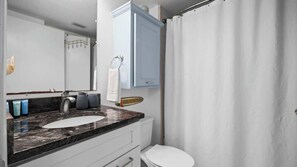 A modern bathroom with a marble sink, a toilet, a shower curtain, and a cabinet above the sink. - Hot Tub•Oceanfront •Heated Pools•King•Cable TV•W/D (Orange Beach)