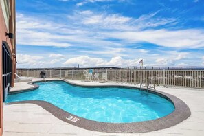 A swimming pool with a curved design, surrounded by a fence and a deck area with chairs. - Hot Tub•Oceanfront •Heated Pools•King•Cable TV•W/D (Orange Beach)