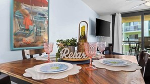 A dining table set with plates, glasses, and a bottle of wine. A sign with the word "Relax" is visible. - Hot Tub, Oceanfront, Heated Pools, King, Cable TV, W/D (Orange Beach)