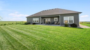 A single-story house with a covered patio, a lawn, and a clear sky.