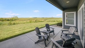 A patio with four Adirondack chairs and a table, overlooking a well-maintained lawn and distant hills.