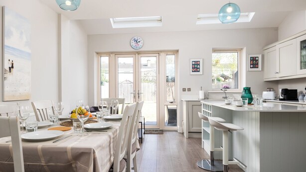 Una cocina moderna con una isla central, armarios blancos y una zona de comedor con una mesa para cuatro.