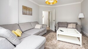 Una sala de estar con dos sofás grises, una mesa de centro blanca, un tapete mullido y un cuadro en la pared.