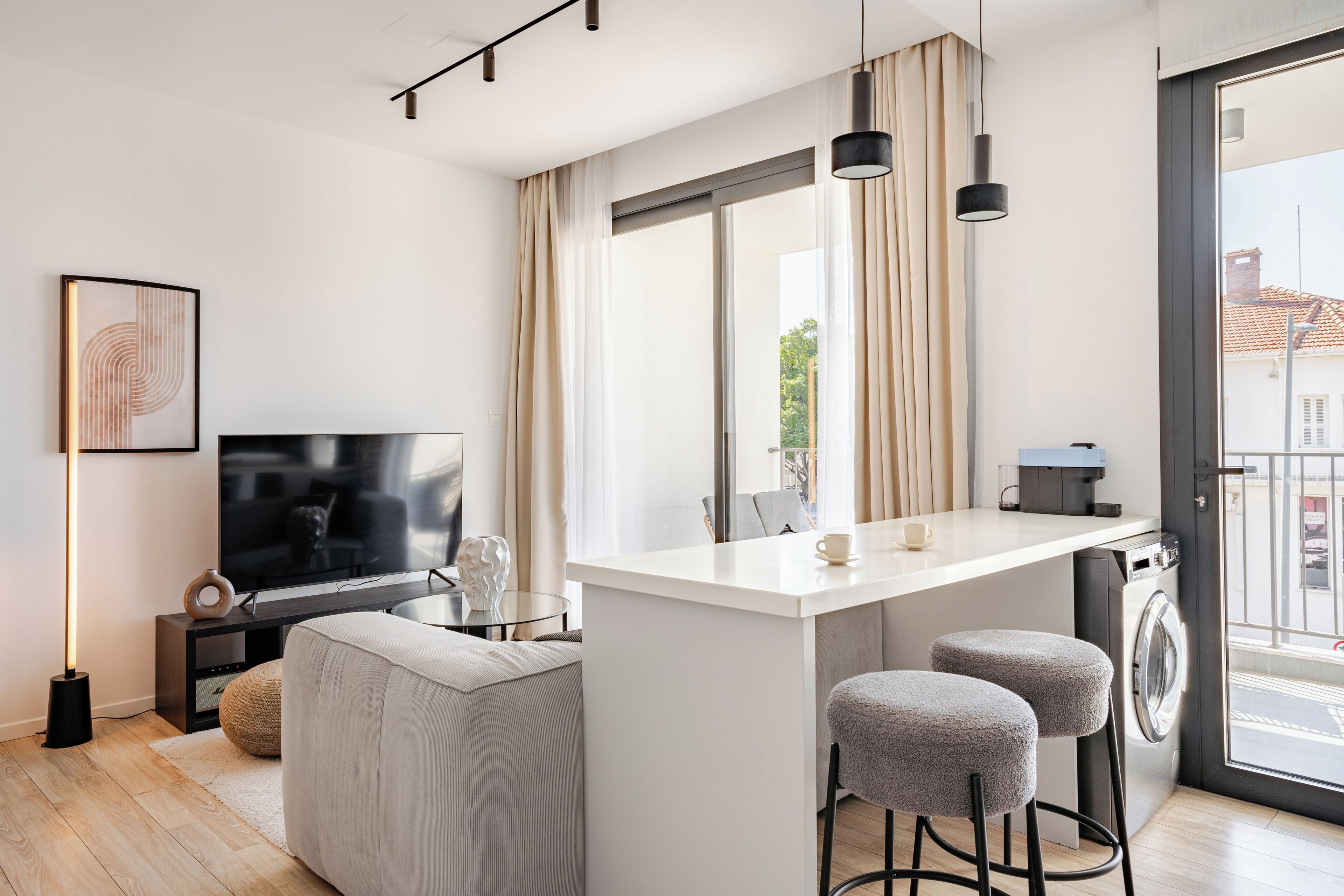A modern living room with a flat-screen TV, a sofa, a coffee table, and a dining area with stools.