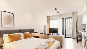 Una habitación de hotel moderna con una cama grande, televisión, sofá y una zona de cocina.