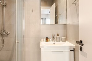 A bathroom with a glass shower enclosure, a white sink with toiletries, and a mirror above the sink. - Yamas Urban Living Olympia Suites (Limassol)