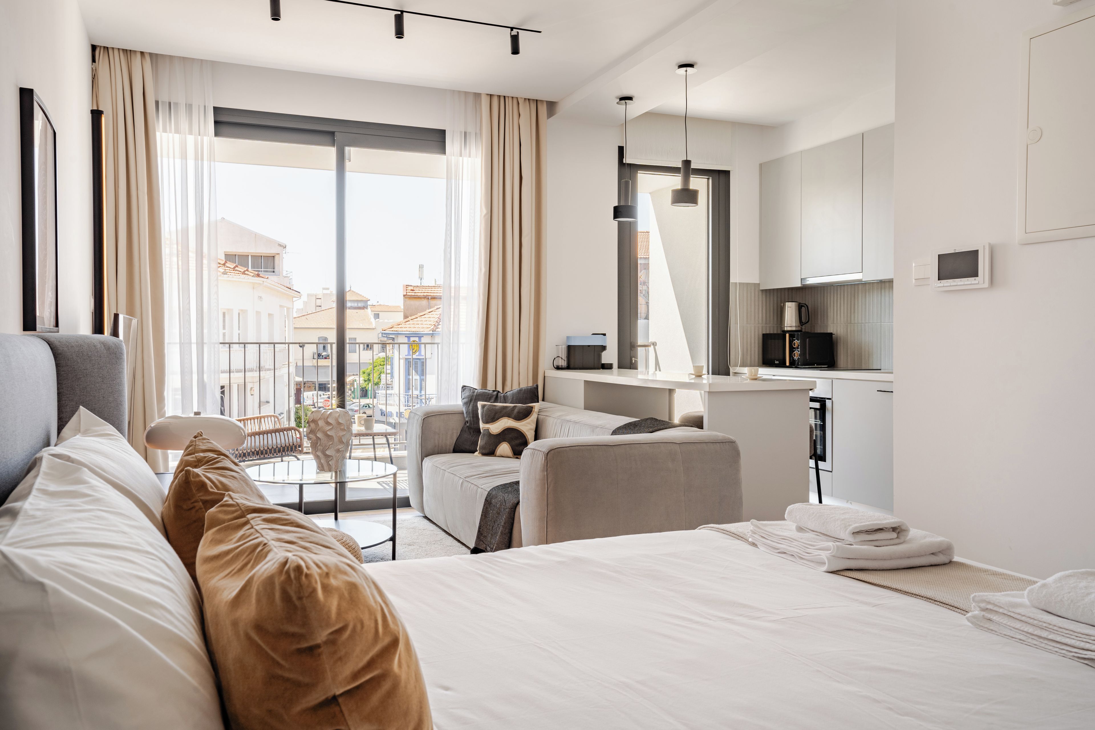Habitación de hotel moderna con cama, zona de estar, kitchenette y vistas a la ciudad.