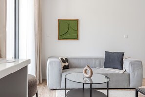 A modern living room with a striped sofa, a round glass table, and a minimalist green abstract painting on the wall. - Yamas Urban Living Olympia Suites (Limassol)