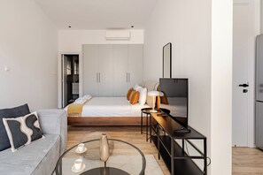 A modern bedroom with a bed, bedside table, lamp, and a TV. - Yamas Urban Living Olympia Suites (Limassol)