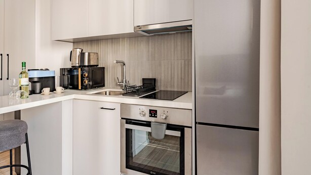 Een kleine keuken met een ingebouwde oven, een koffieapparaat en een roestvrijstalen koelkast.