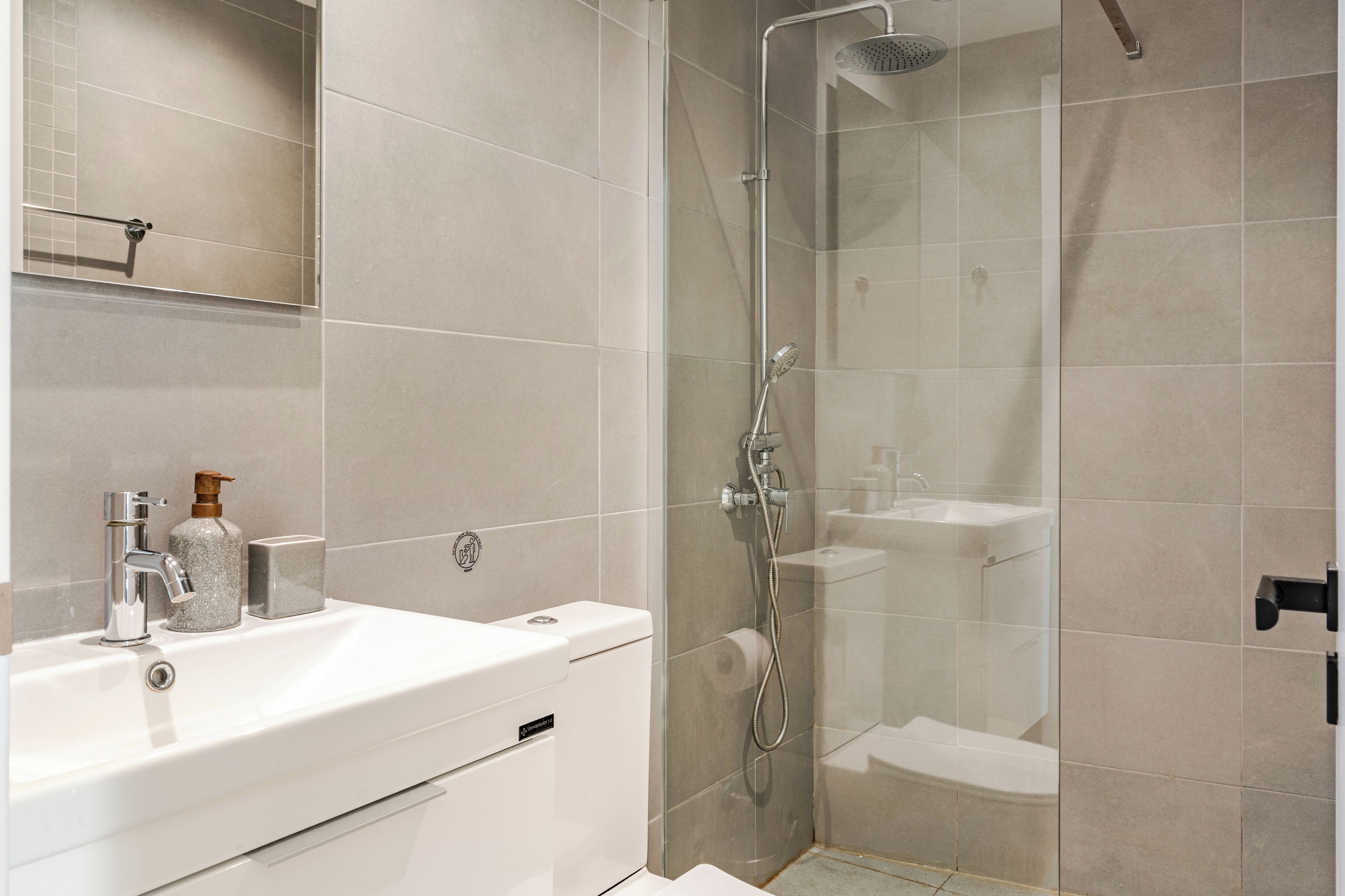 Un baño moderno con ducha envuelta en vidrio, un lavabo blanco y un espejo sobre el lavabo.