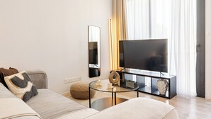 Una sala de estar moderna con un sofá, una mesa de centro de vidrio, un televisor de pantalla plana y una mesita auxiliar con objetos decorativos.