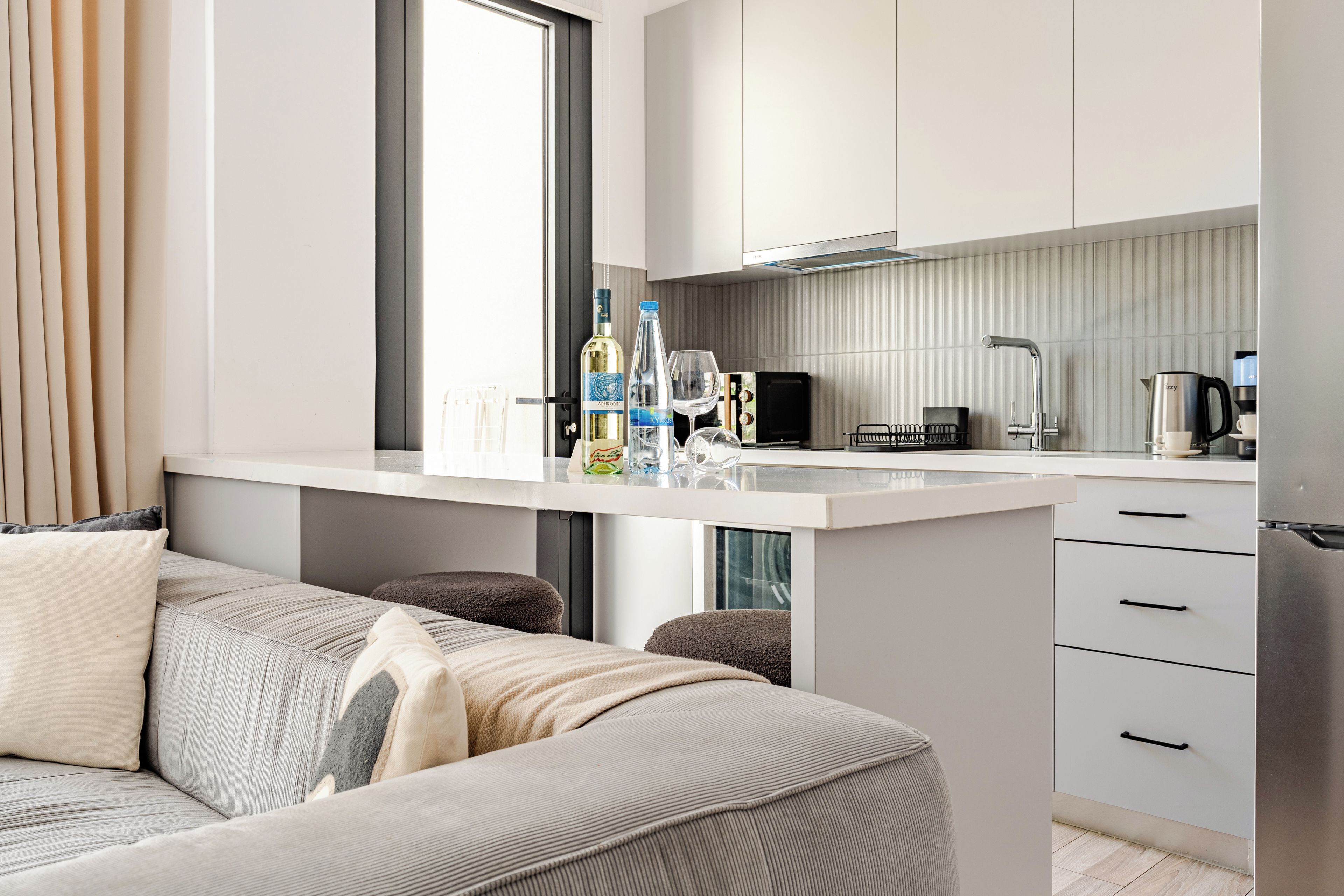 A modern kitchen with a central island, a dining area with a sofa, and a view through a window.
