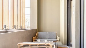Ein Balkon mit Korbmöbeln, einem kleinen Tisch und Blick auf ein Gebäude.