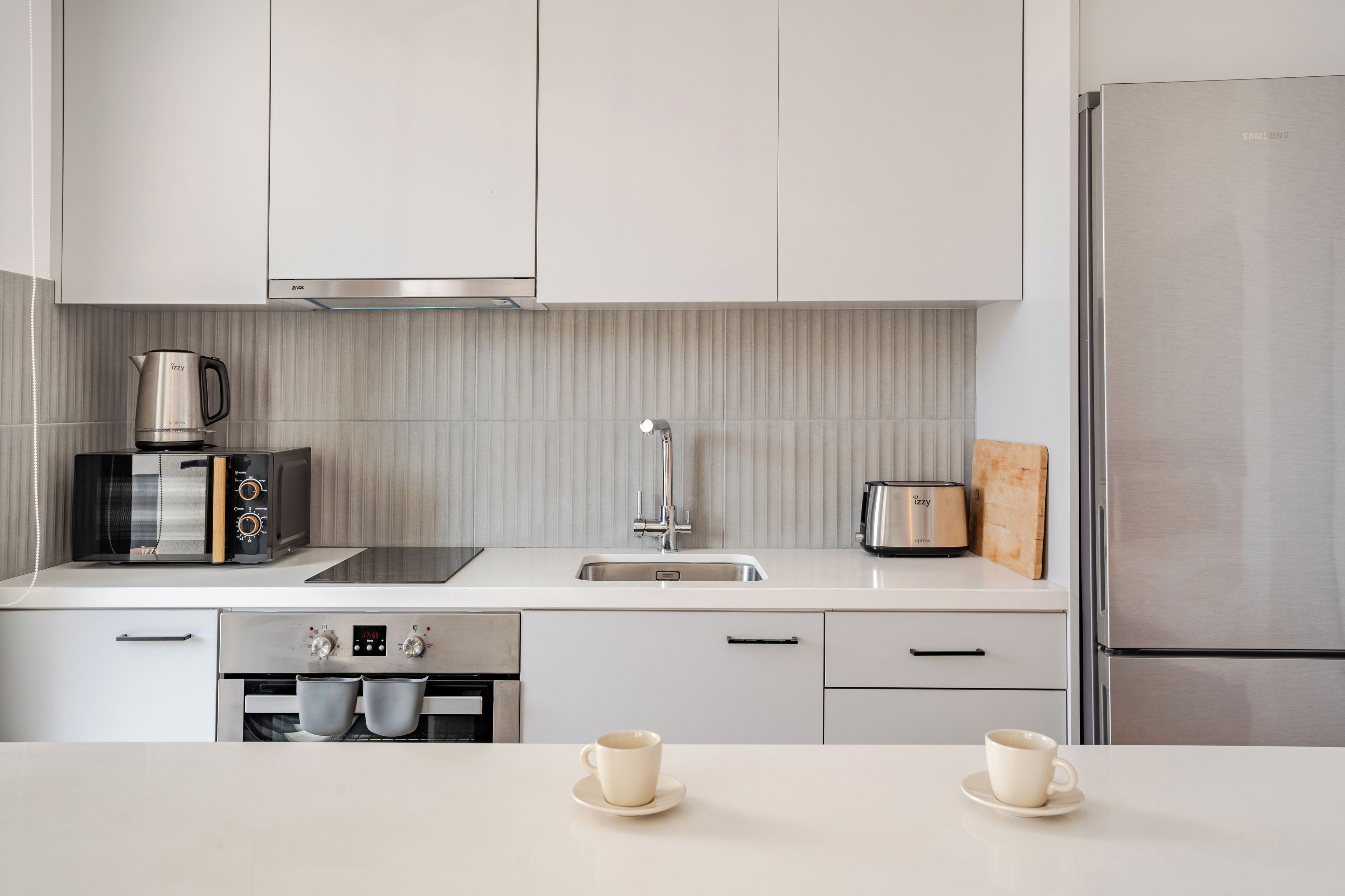 A modern kitchen with white cabinetry, a stainless steel refrigerator, a coffee maker, and a toaster.
