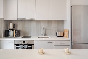 A modern kitchen with white cabinetry, a stainless steel refrigerator, a coffee maker, and a toaster. - Yamas Urban Living Olympia Suites (Limassol)