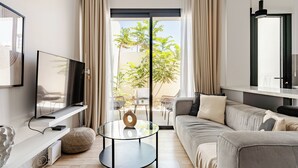 Een moderne woonkamer met een flatscreen televisie, een ronde glazen salontafel, een bank en uitzicht op het groen door een schuifpui.