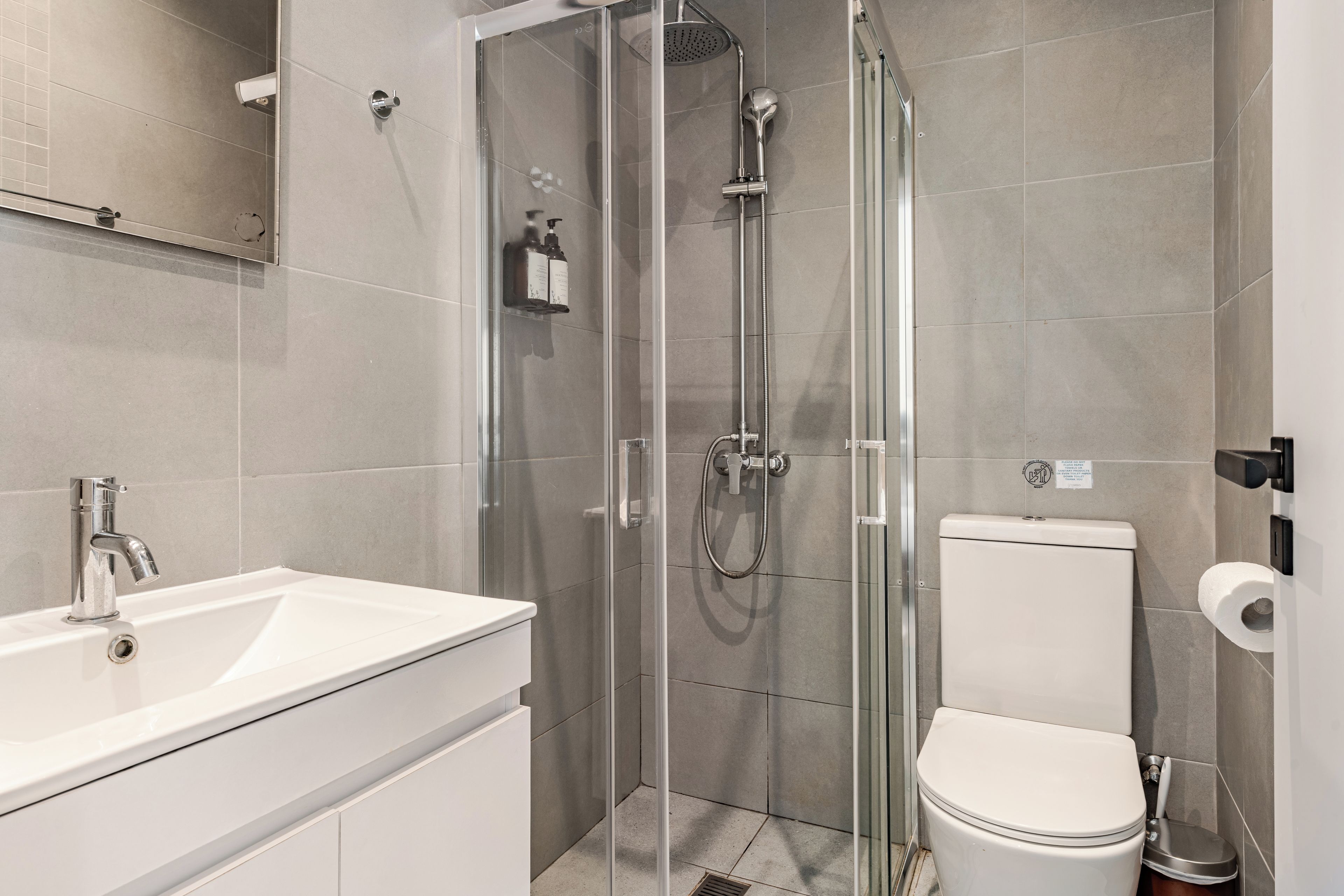 A modern bathroom with a glass-enclosed shower, a white sink, and a toilet.