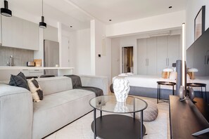 Een moderne hotelkamer met een bank, een glazen bijzettafeltje, een bed met hoofdeinde, een nachtkastje met lampen en een grote spiegel.