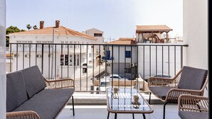 Een balkon met rieten meubels, een glazen tafel en uitzicht op de straat en gebouwen.
