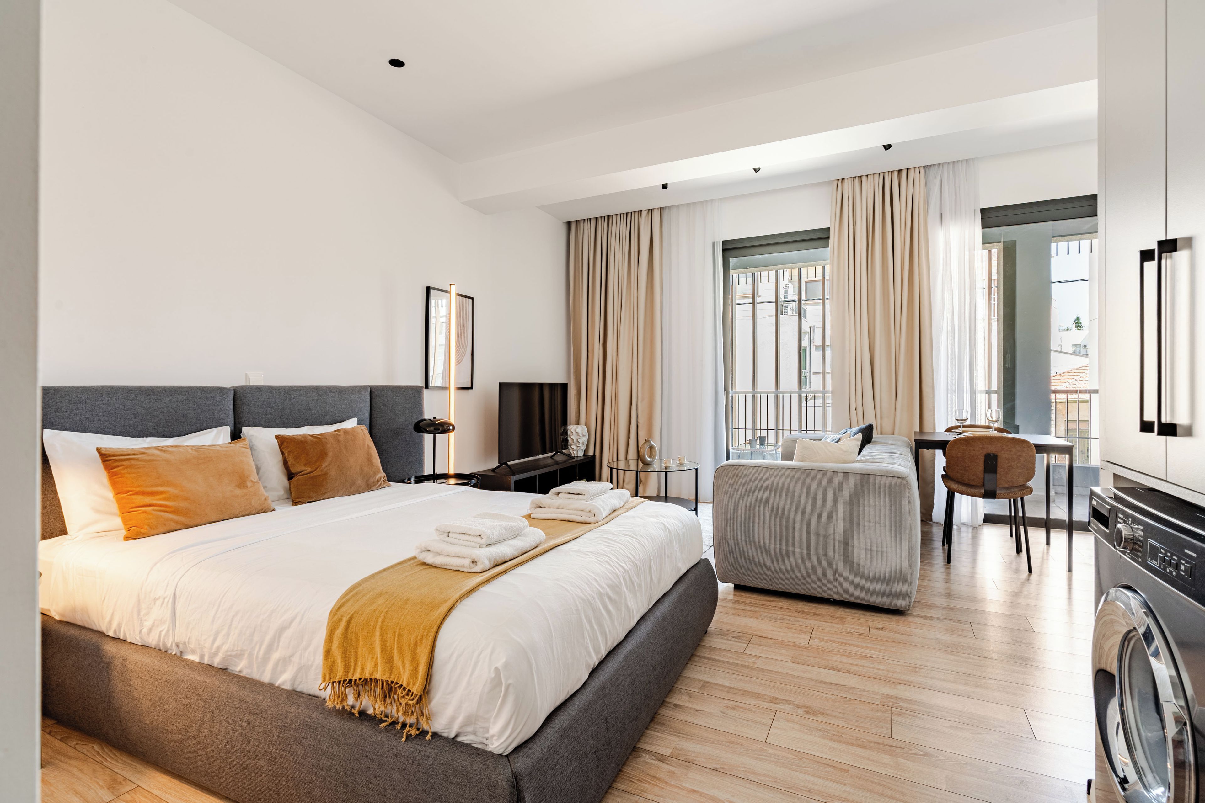 Una habitación de hotel moderna con una cama grande, un sofá, un comedor y una lavadora.