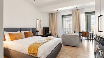 Una habitación de hotel moderna con una cama grande, un sofá, un comedor y una lavadora.