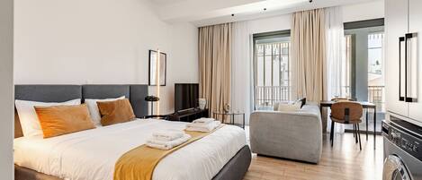 Una habitación de hotel moderna con una cama grande, un sofá, un comedor y una lavadora.