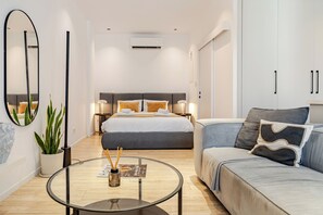 Quarto de hotel moderno com cama, sofá, mesa de centro e planta em vaso.