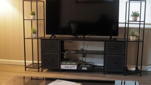 A flat-screen TV on a black TV stand with two drawers and a shelf, placed in a room with wooden walls and a window. - Modern Luxury 1BR Prime Location by Oakley, Rookwood, Downtown & Top Hospitals (Norwood)