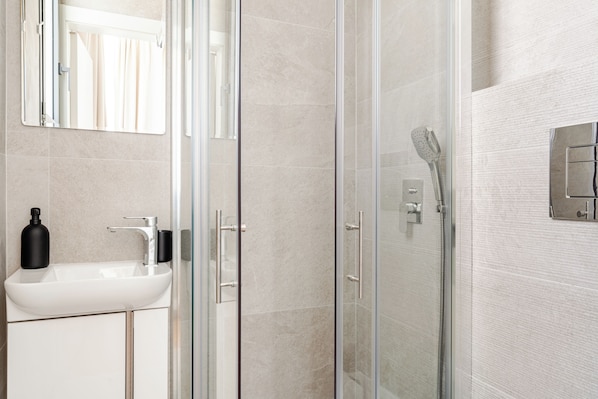 Ein modernes Badezimmer mit einer Duschkabine aus Glas, einem weißen Waschbecken und einem Spiegel darüber.