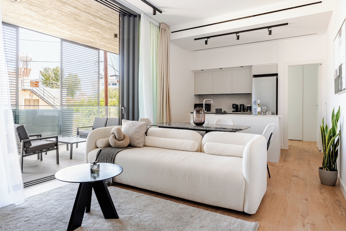 Ein modernes Wohnzimmer mit einer Couch, einem Couchtisch und einem Essbereich mit einer Küche im Hintergrund.