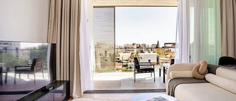 A modern living room with a sofa, a coffee table, a TV, and a balcony with a view of the city.