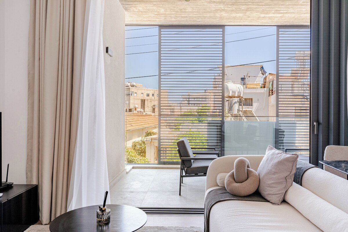 A modern living room with a sofa, a coffee table, and a view of the city through large windows.