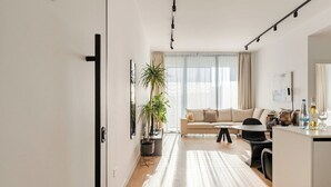 A modern living room with a sofa, a dining table, and a kitchen area. - Yamas Urban Living Sequoia Residence (Limassol)