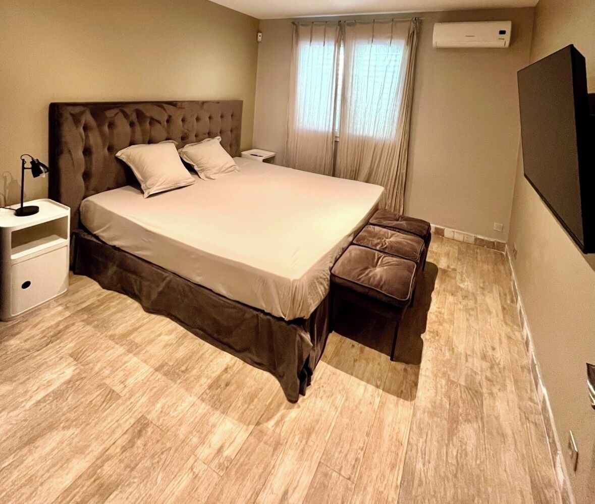 Un dormitorio moderno con una cama grande, una mesita de noche, un banco y un equipo de aire acondicionado.