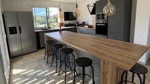 Una cocina moderna con una isla de madera, taburetes de bar, electrodomésticos de acero inoxidable e iluminación colgante.