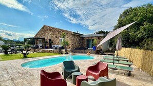 Un área de piscina con mobiliario moderno para exteriores, un edificio de piedra y un cielo despejado.