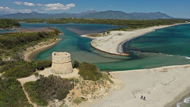 Un paisaje costero con una playa arenosa, una torre y una bahía de aguas cristalinas.