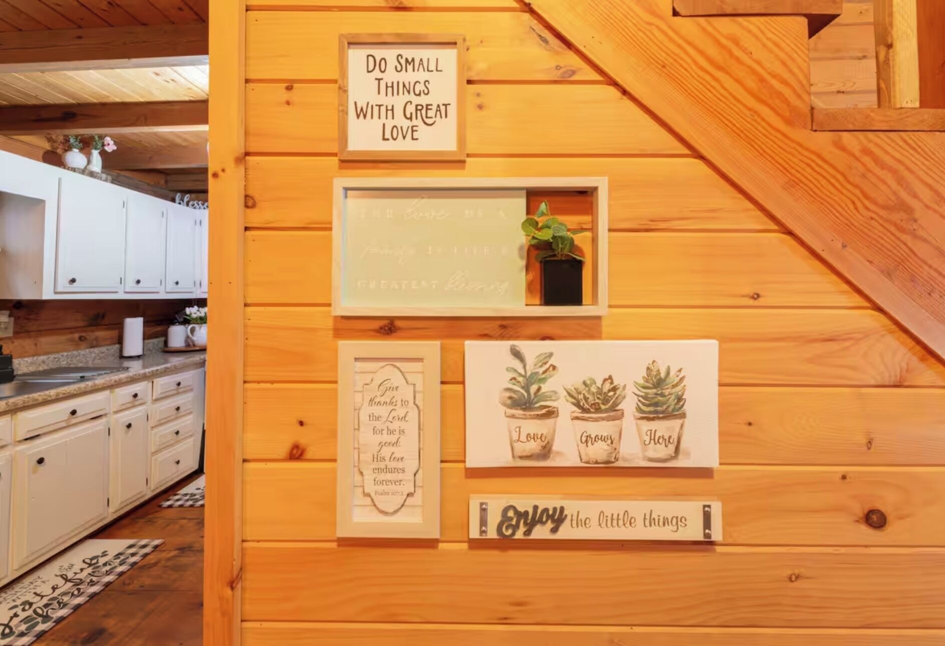 A wooden interior with a kitchen area, a sign saying "Do small things with great love," and framed inspirational quotes.