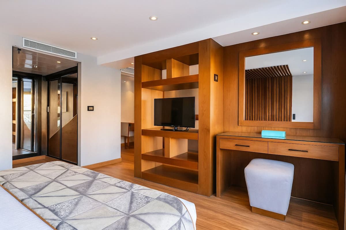 A modern hotel room with a large bed, a TV, a wooden desk, and a mirror.