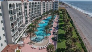 Een hotel met een groot zwembadgedeelte, meerdere balkons en uitzicht op de oceaan.