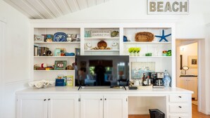 A white kitchen with a built-in TV, shelves with various items, and a 'BEACH' sign above.