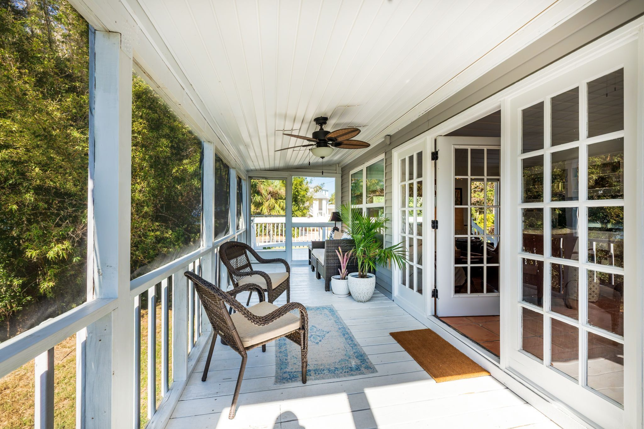 A covered porch with wicker chairs, a ceiling fan, and a view of the outdoors.