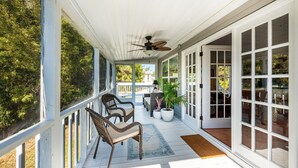 A covered porch with wicker chairs, a ceiling fan, and a view of the outdoors.