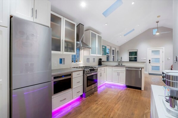 Una cocina moderna con electrodomésticos de acero inoxidable, armarios blancos y piso de madera.