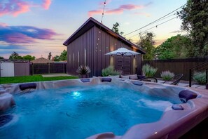 Un jacuzzi con cubierta de madera, rodeado de mobiliario exterior y una zona de estar techada.