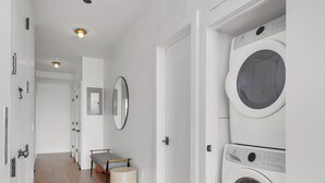 A laundry room with two stacked washing machines, a bench, a mirror, and a door leading to another room.