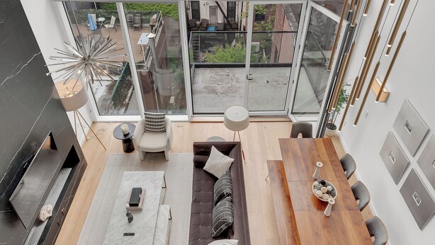 A spacious living area with a large window, a wooden dining table, a sofa, and a fireplace.